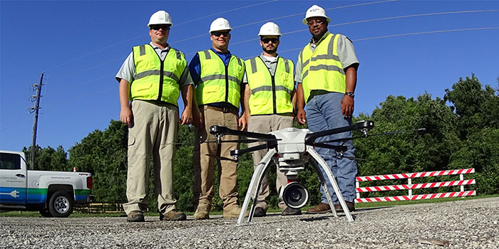 4 Employees facing camera in front of drone